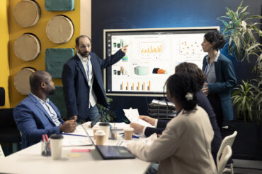 Marketing team attending an important meeting to review sales trends on interactive board, looking to increase organizational revenue and profit. PR specialists ensure global success.